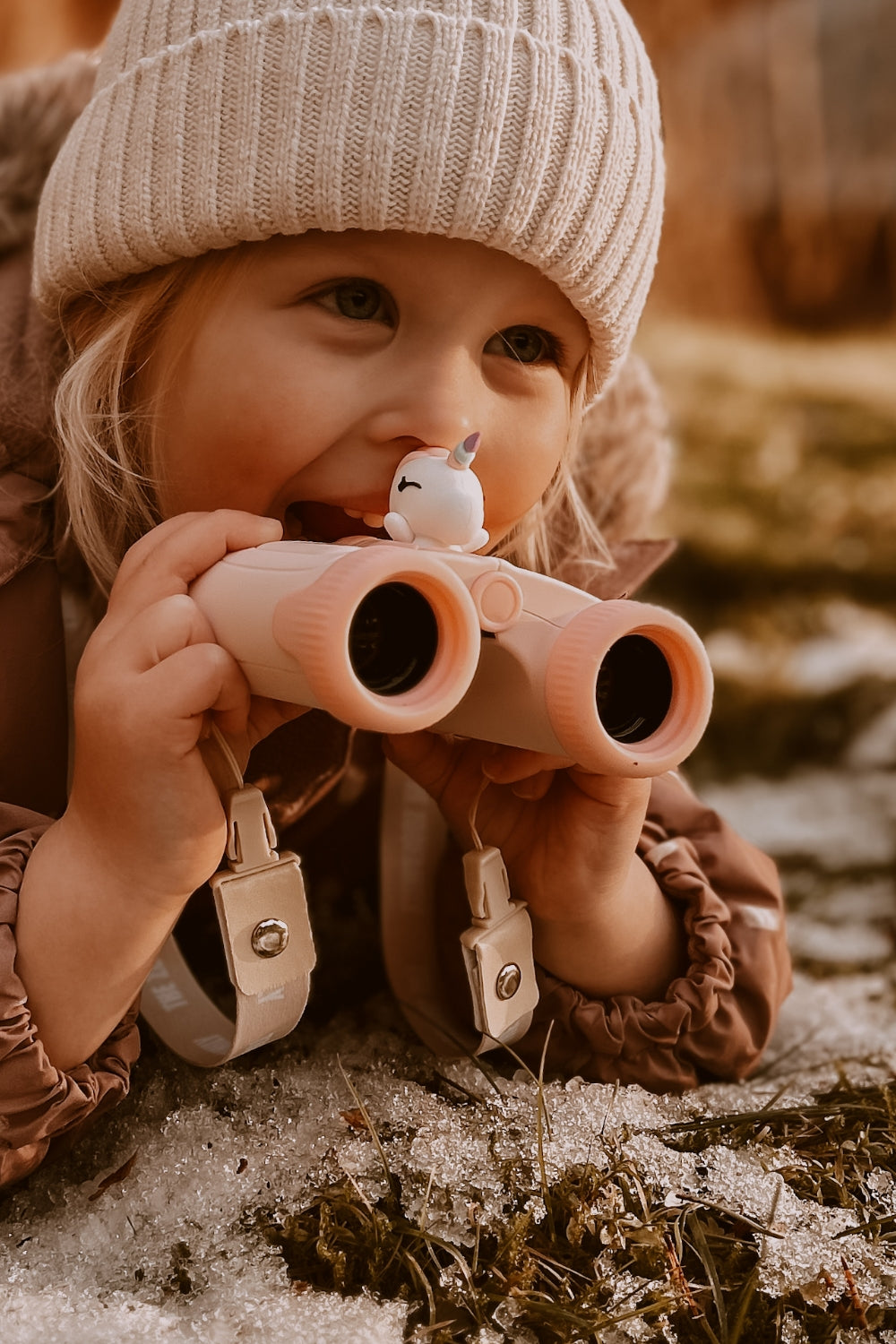 A girl is lying and smiling on the ground, holding the binoculars.